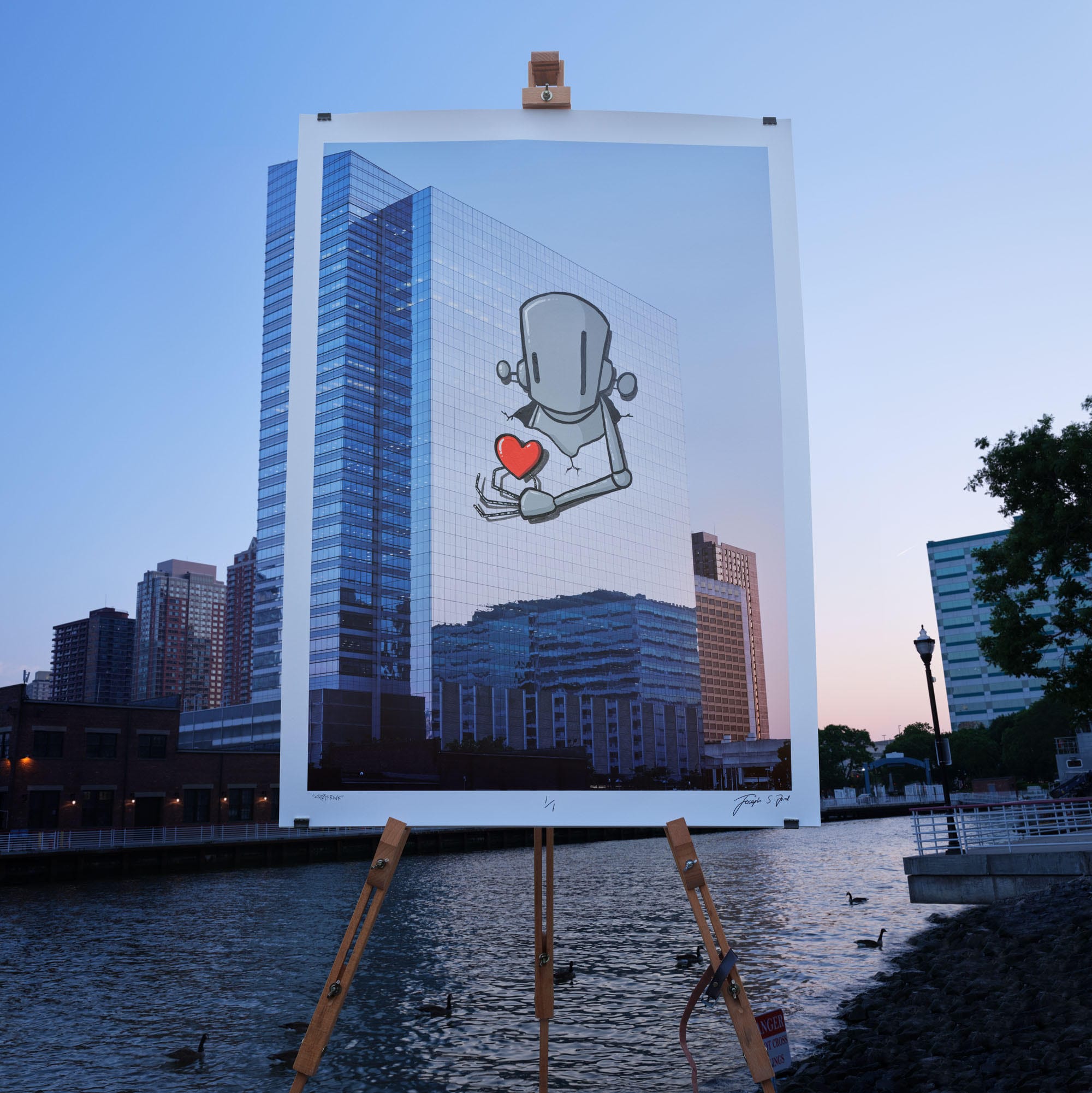 A photographic print of a city and river at sunset with a street art intervention superimposed in the sky, photographed on an easel in front of the same landscape