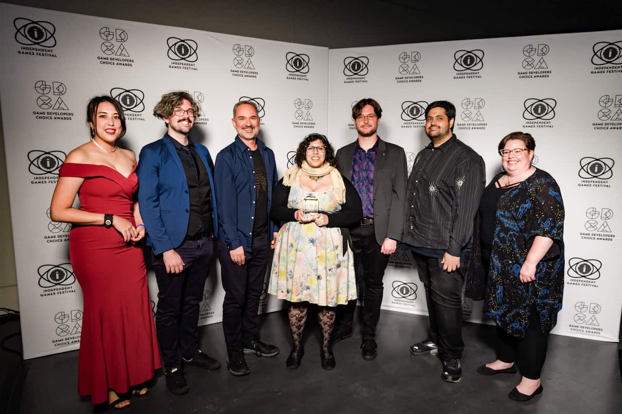 A group of people standing in front of a large mural that says "Game Developers Choice Awards".