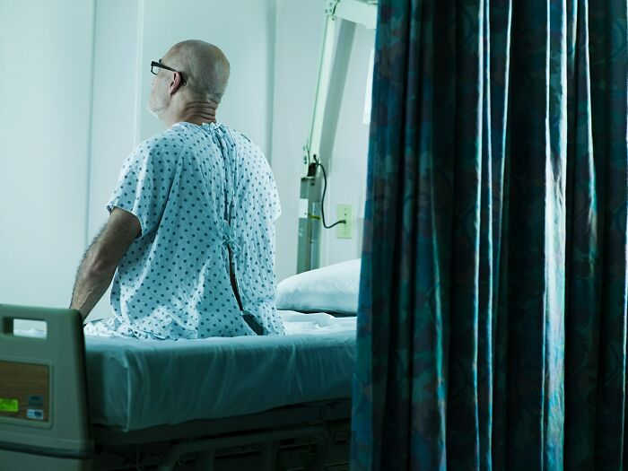 Elderly patient in hospital gown sitting on bed, highlighting hidden hospital truths that may be unsettling for visitors.