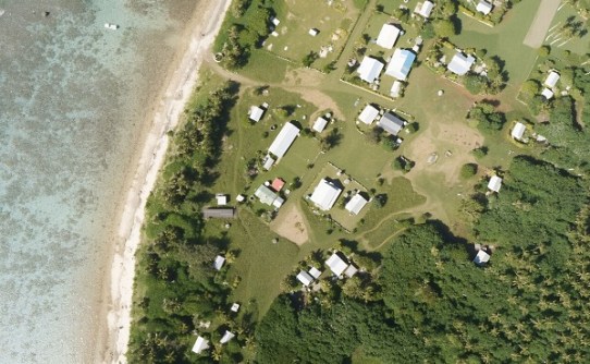 A aerial photo of a shoreline, showing the roofs of houses and sheds quite near the water