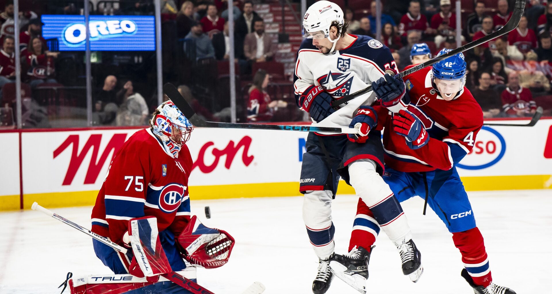 Hockey goaltender makes a save while an opponent and defender clash in front of the net.