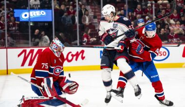 Hockey goaltender makes a save while an opponent and defender clash in front of the net.