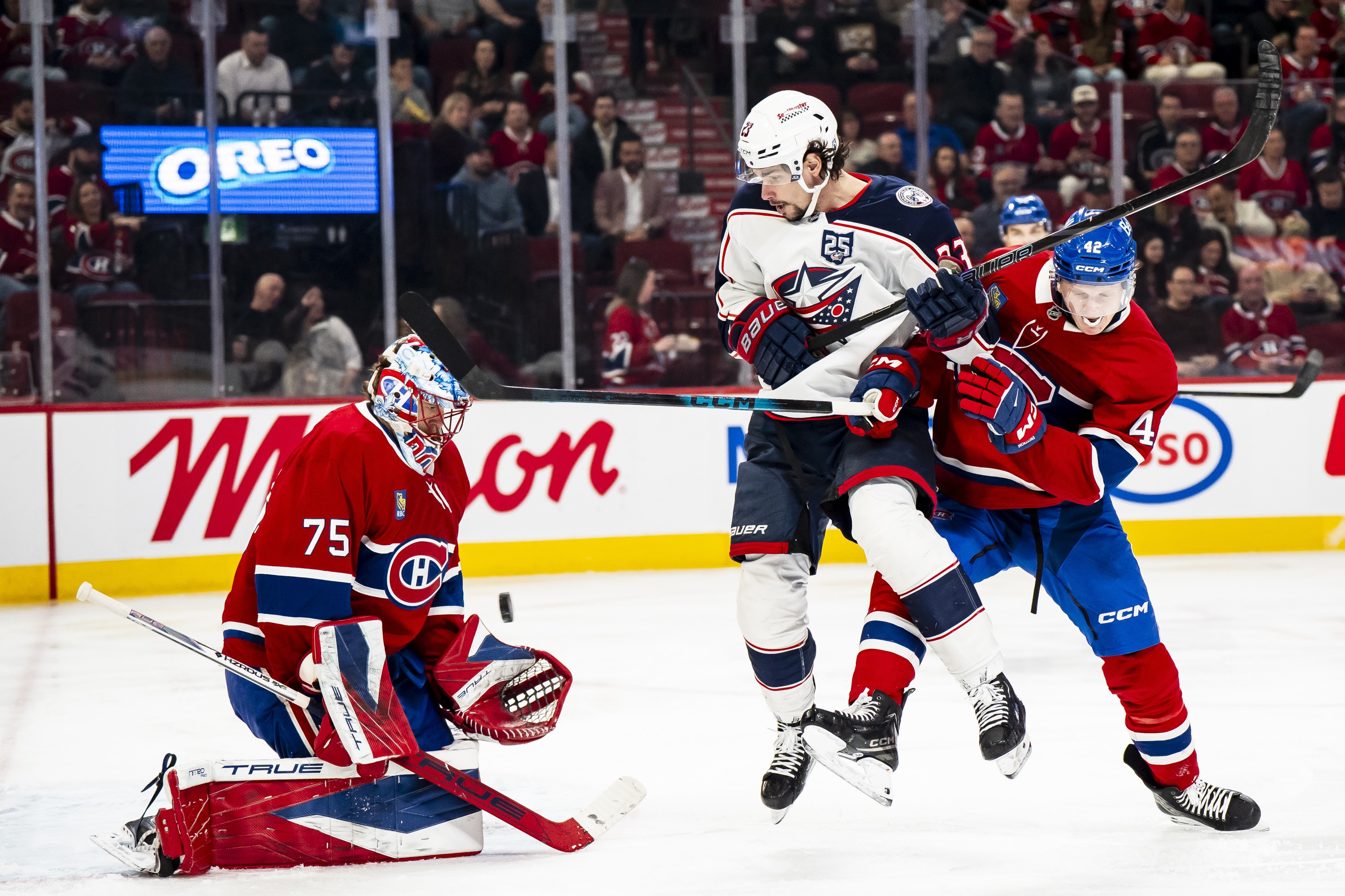 Hockey goaltender makes a save while an opponent and defender clash in front of the net.