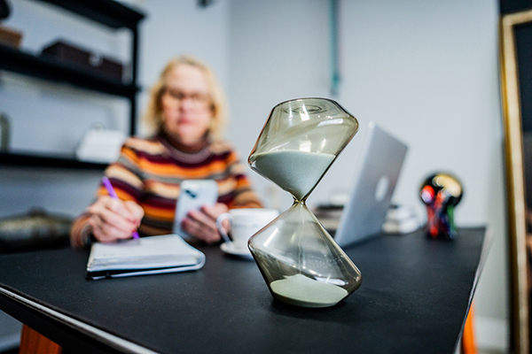 An hourglass beside a woman making notes