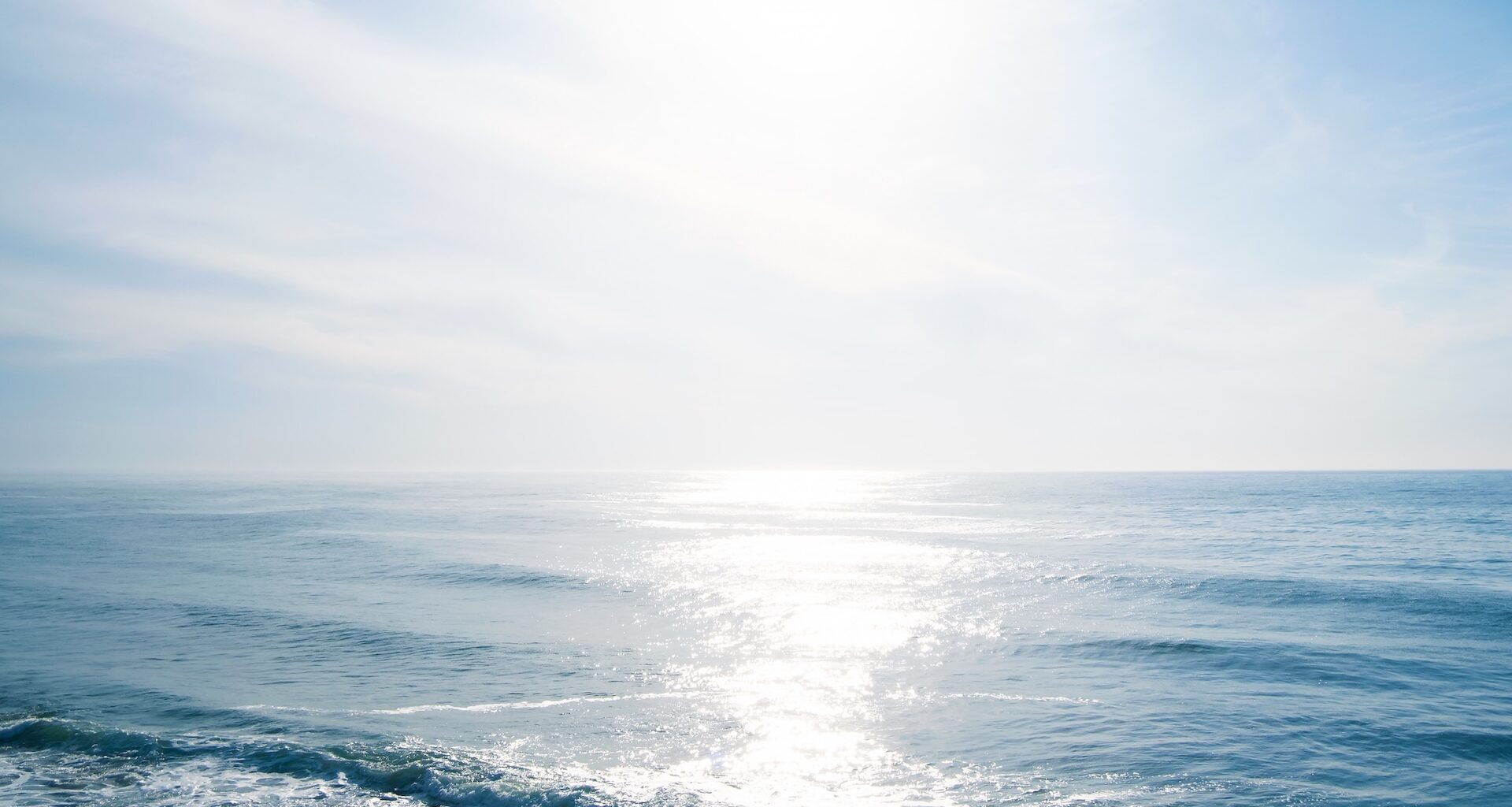 A tranquil seascape with soft waves reflecting sunlight under a bright, clear sky.