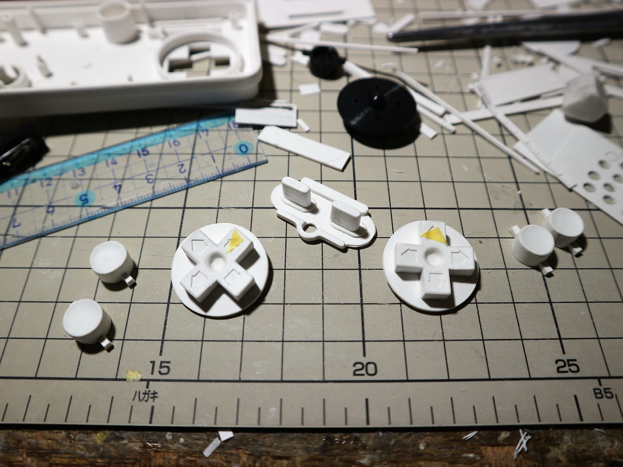 a hyperrealistic, scale sculpture in progress, eventually to depict a game console, shown on a studio table covered in pieces of paper