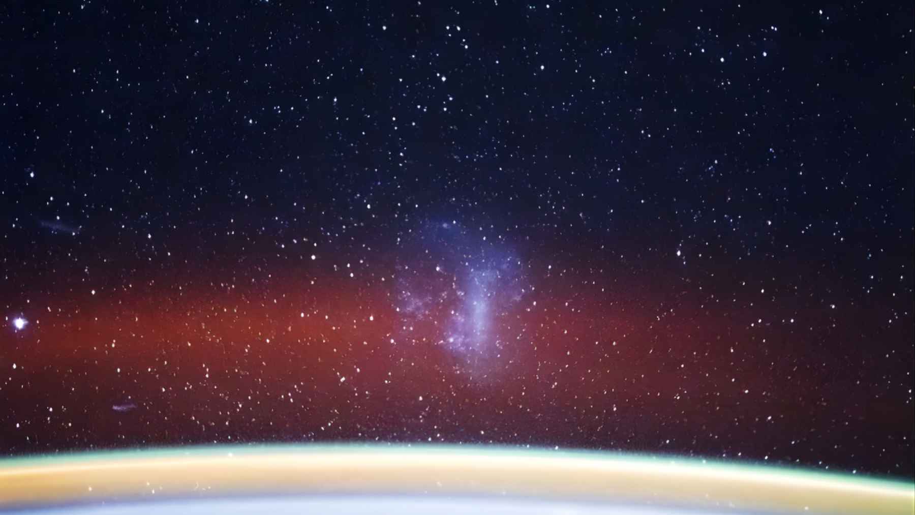 View from the International Space Station showing Earth’s glowing horizon and the Large Magellanic Cloud as a bright patch in a star-filled sky.