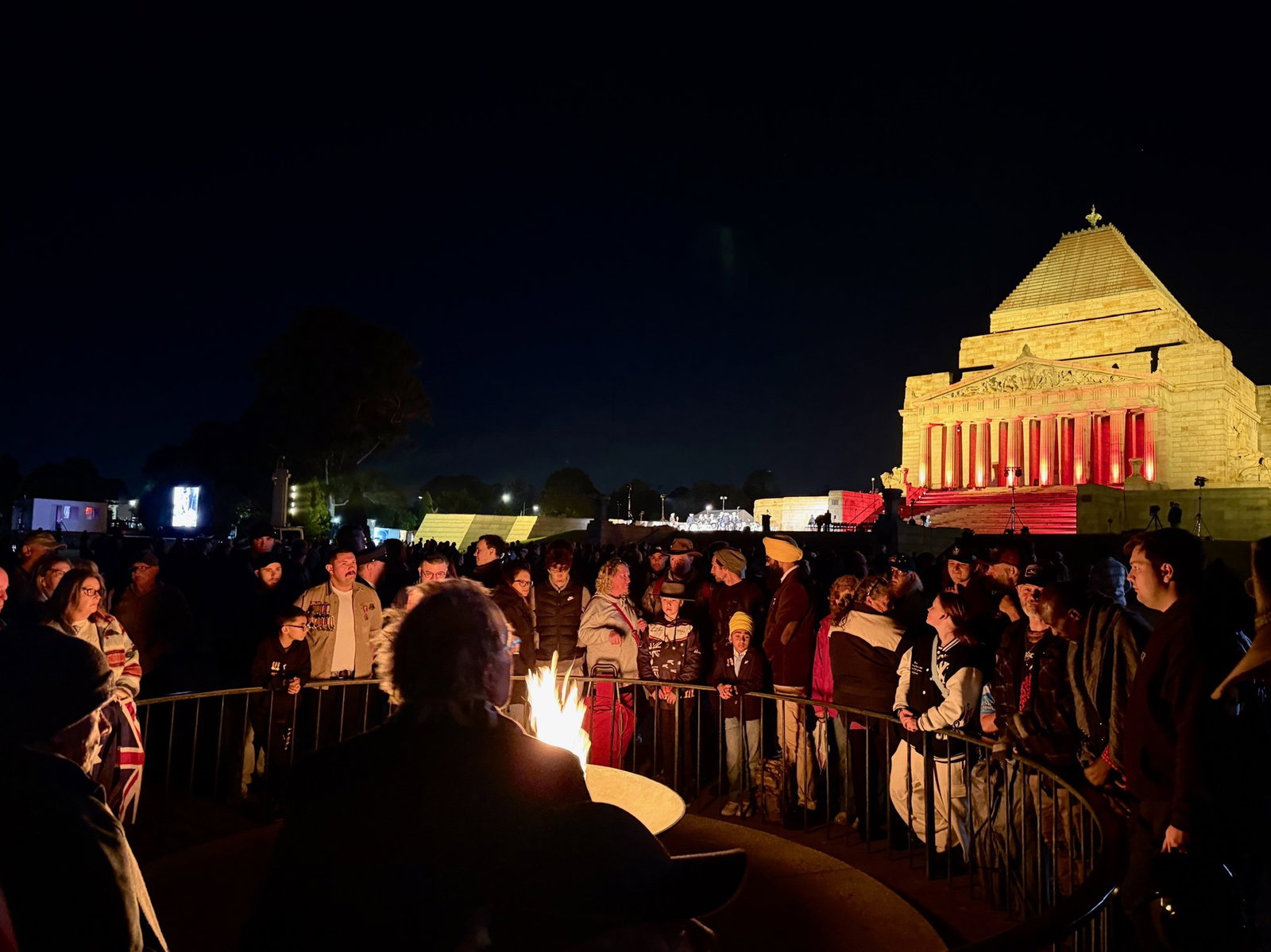 crowd of people gathered around a fire at an anzac service