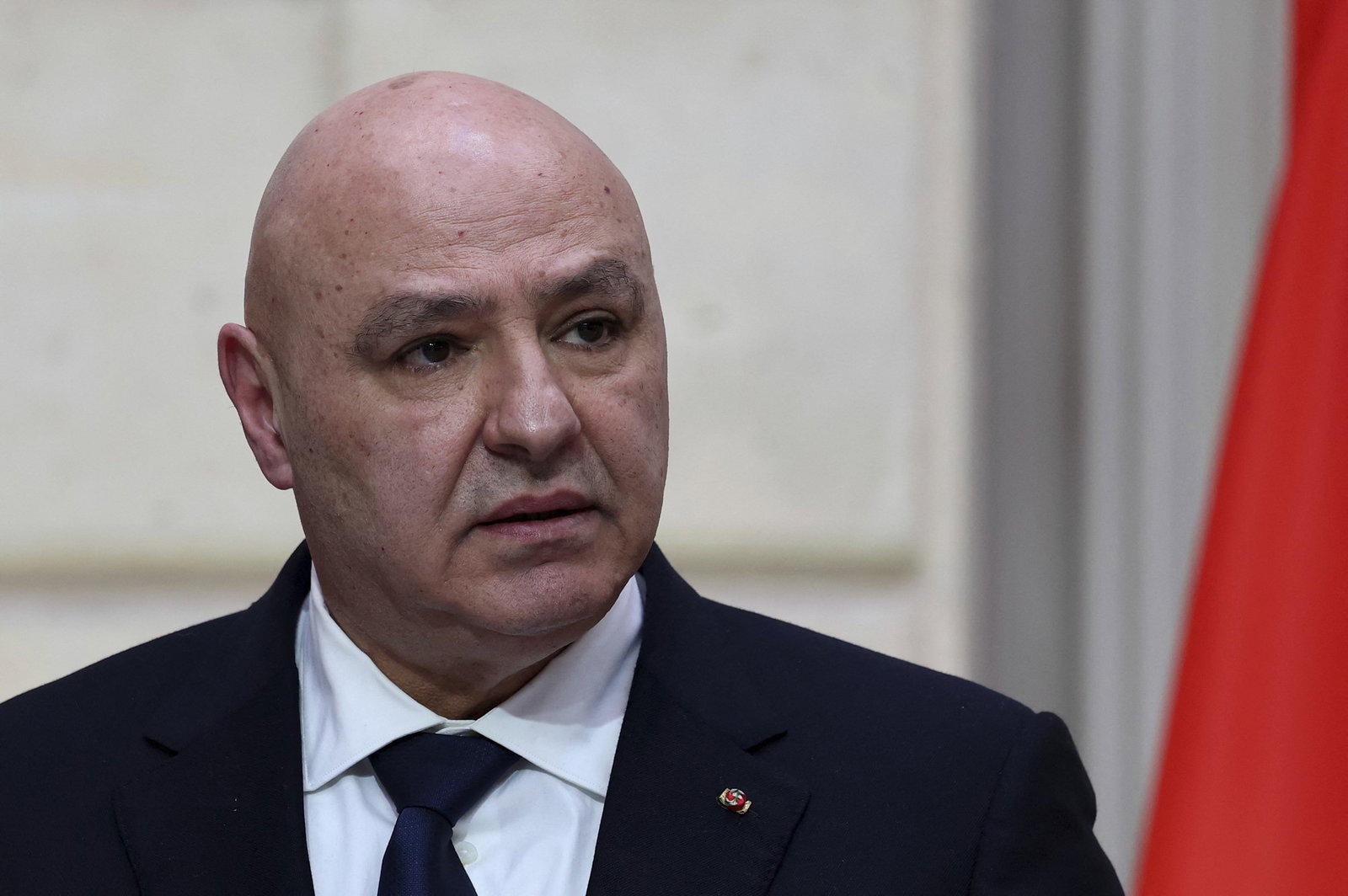 A bald man in a black suit looks to the right of the camera.