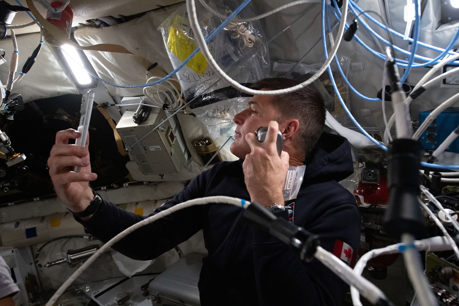 A man shaves inside a spacecraft while filming himself on a phone