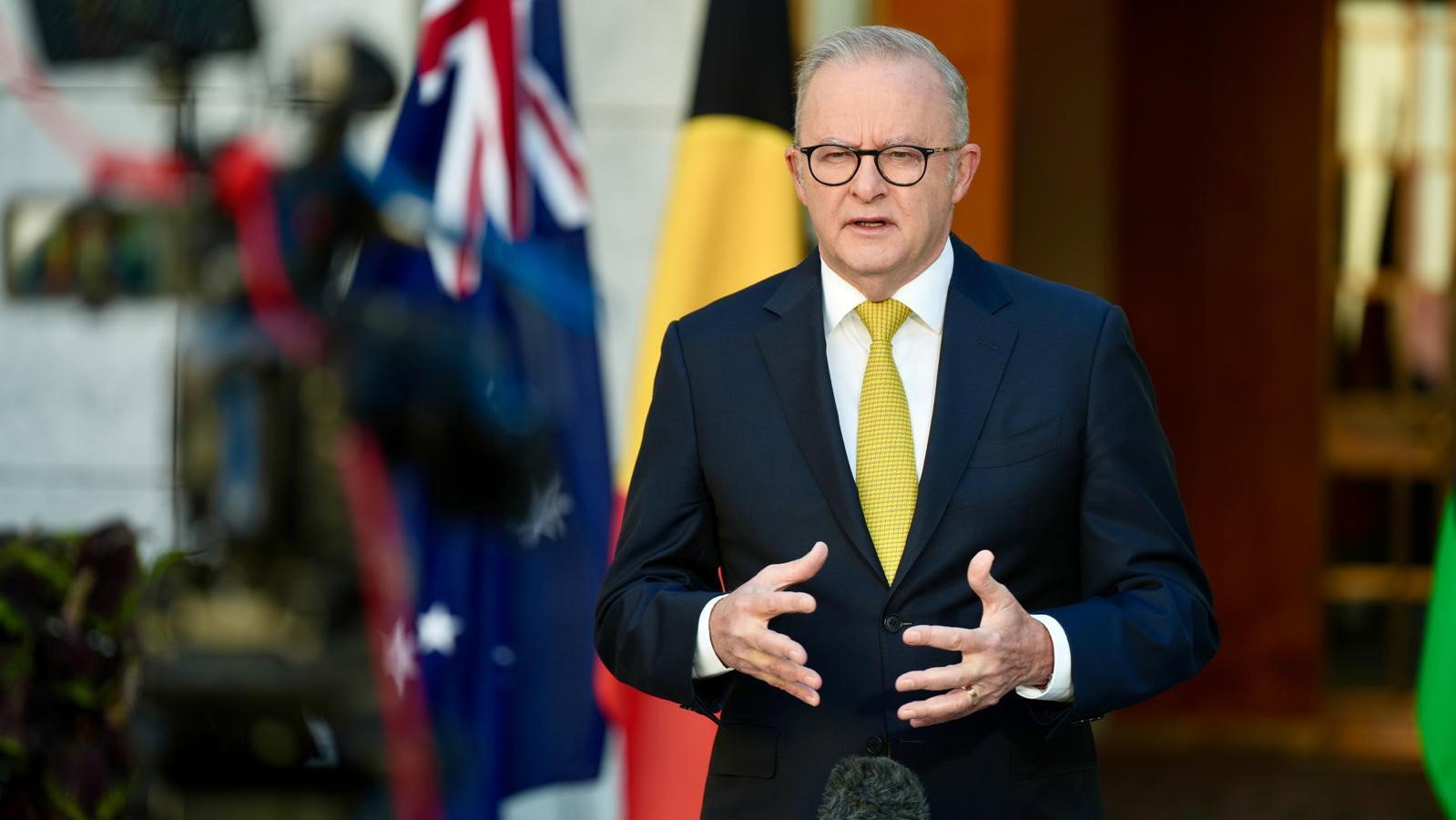 Anthony Albanese is interviewed with flags behind him in the prime minister's courtyard. 