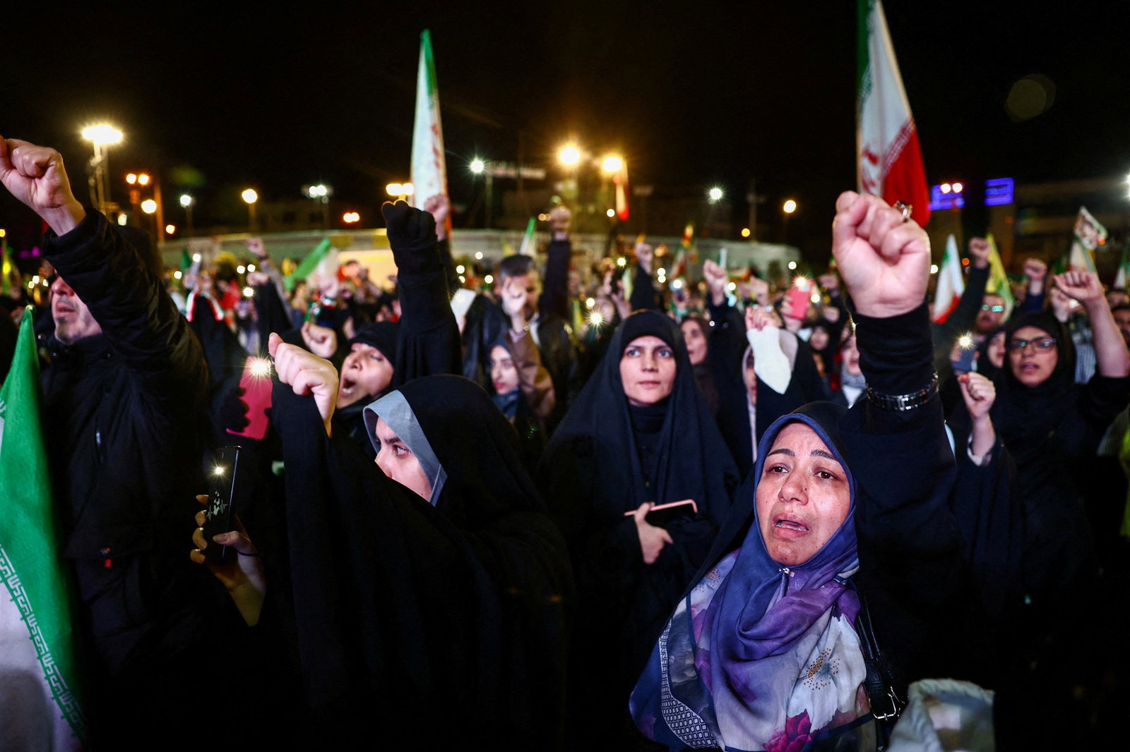 Women wearing headscarves holding Iran flags and holding their fists in the air.