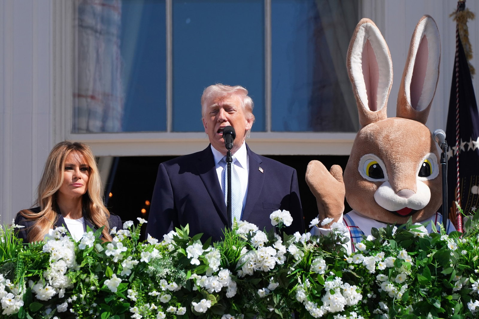 A man speaks into a micraophone as a woman and a person in an Easter bunny costume stand on either side.