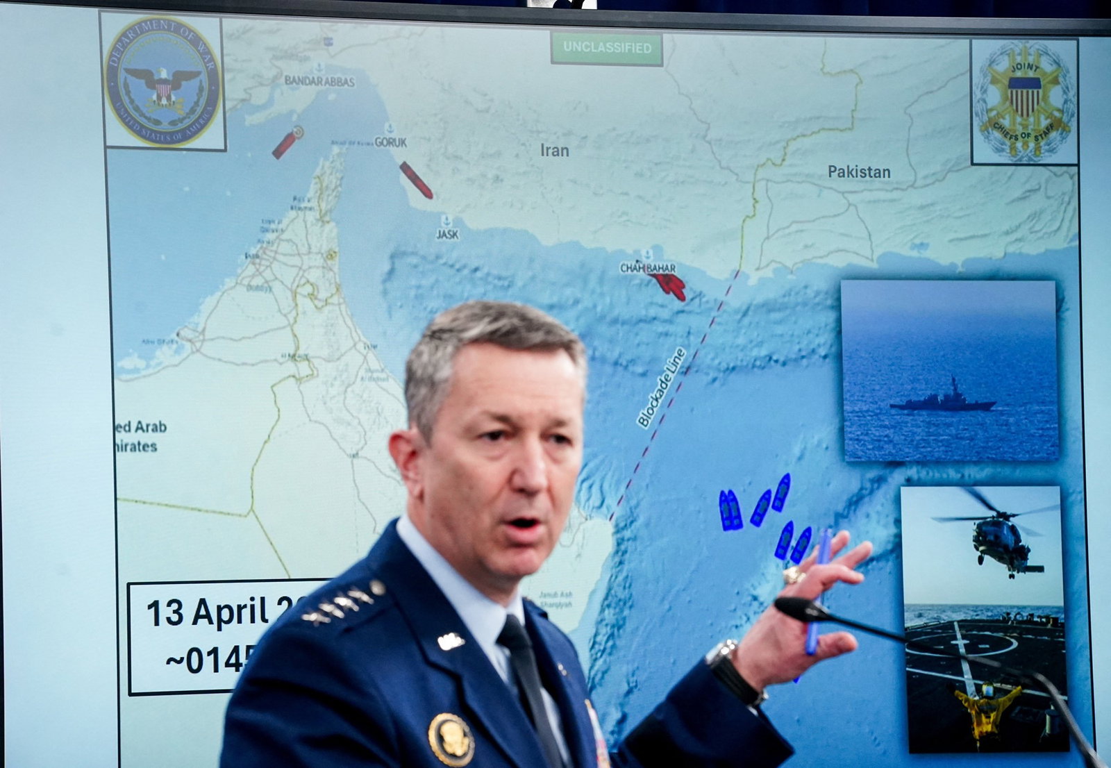 A man standing at a podium in front of a large map of the Strait of Hormuz.