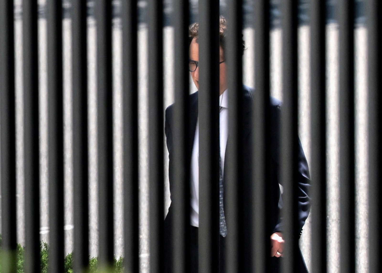 A middle-aged man in a suit is visible through the White House's black fence bars.