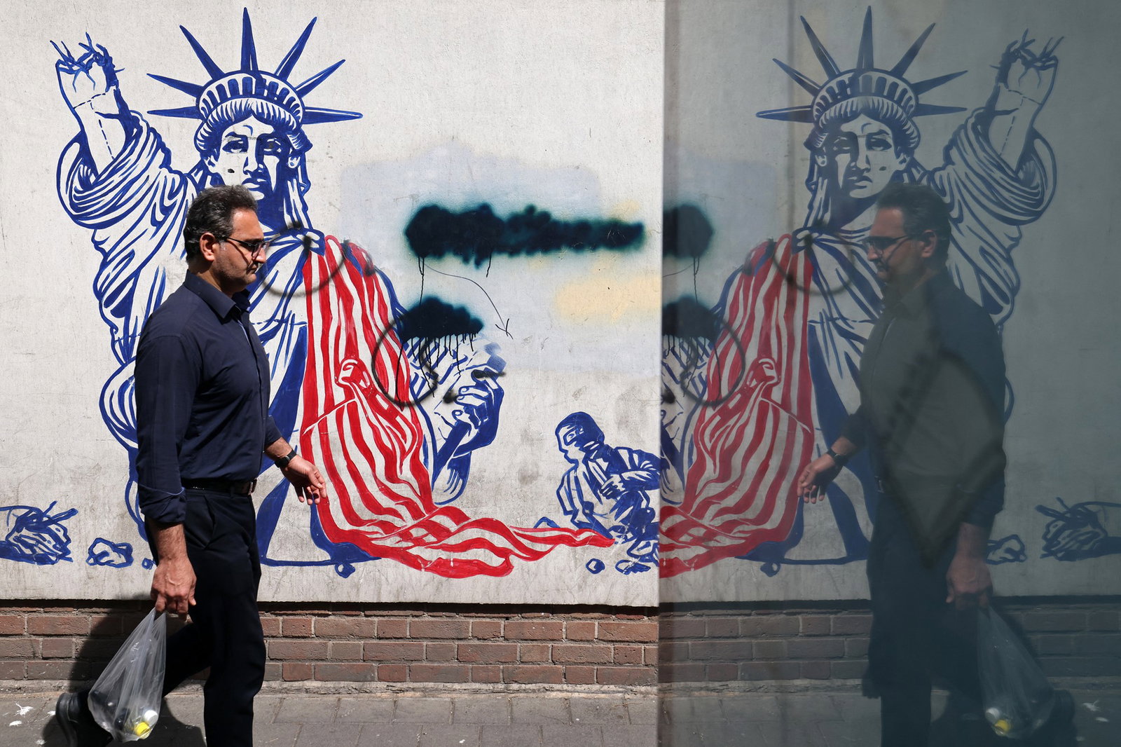 a man walks past a mural depicting a broken statue of liberty
