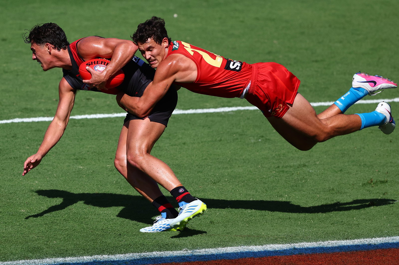 A Suns AFL player tackles a Bombers opponent.