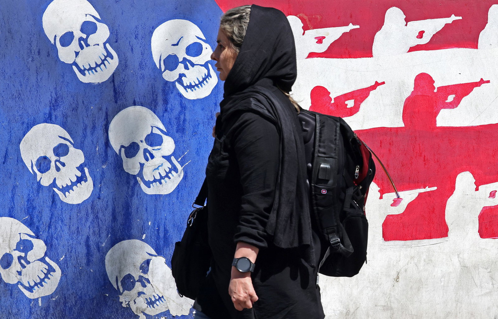 A woman stands in front of a mural that depicts the american flag with skulls and soldiers