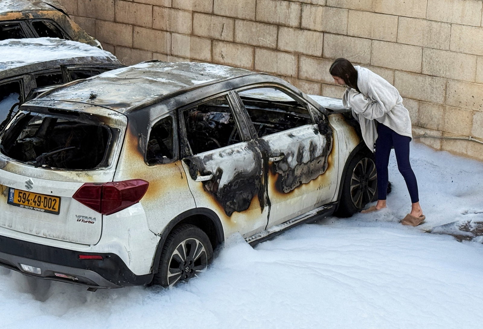 A woman looks at a burnt car. 