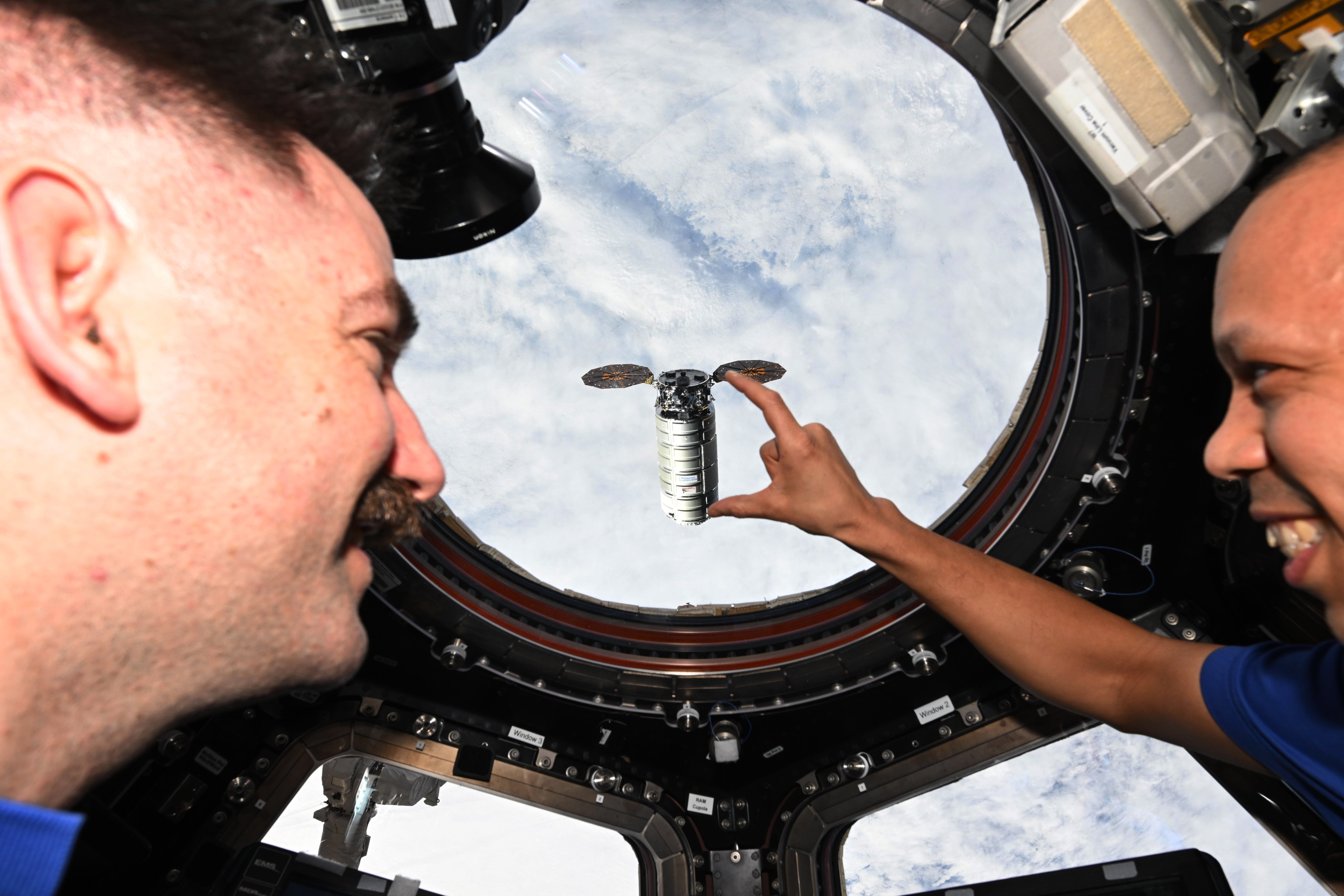 NASA astronauts Chris Williams holds his hand out, appearing to "hold" the Cygnus capsule from the ISS.