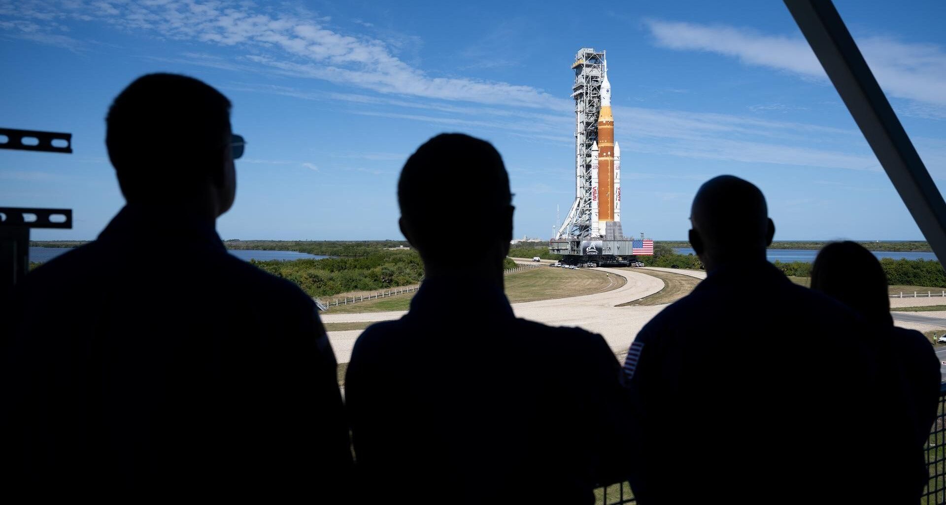 silhouettes of the back of four people looking at an orange rocket.