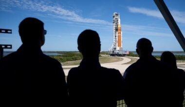 silhouettes of the back of four people looking at an orange rocket.