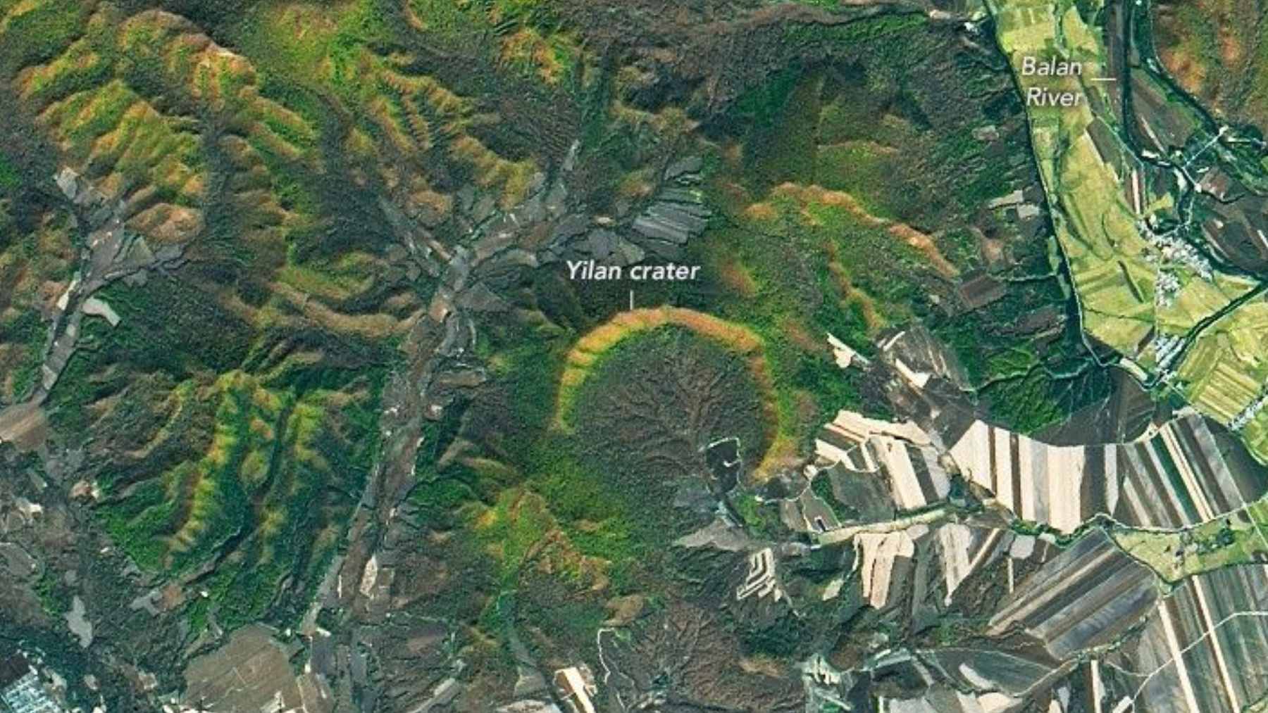 Satellite view of the horseshoe-shaped Yilan impact crater in China, showing the forested rim and central farmlands.
