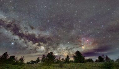 Turbulent, glowing band with dark streaks in it across the sky low along the horizon; trees in the foreground.
