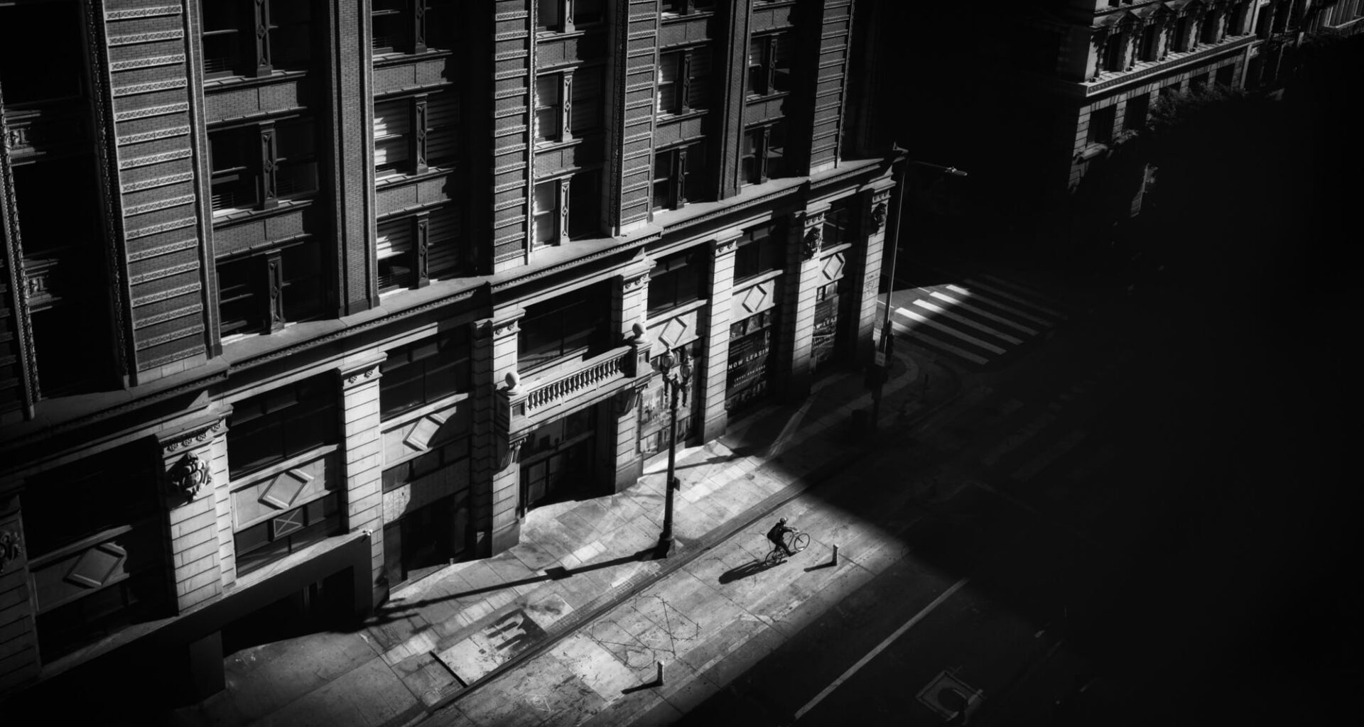 a black-and-white photograph by Daniel Sackheim in a noir style of an elevated city street view with a figure walking amid deep shadows