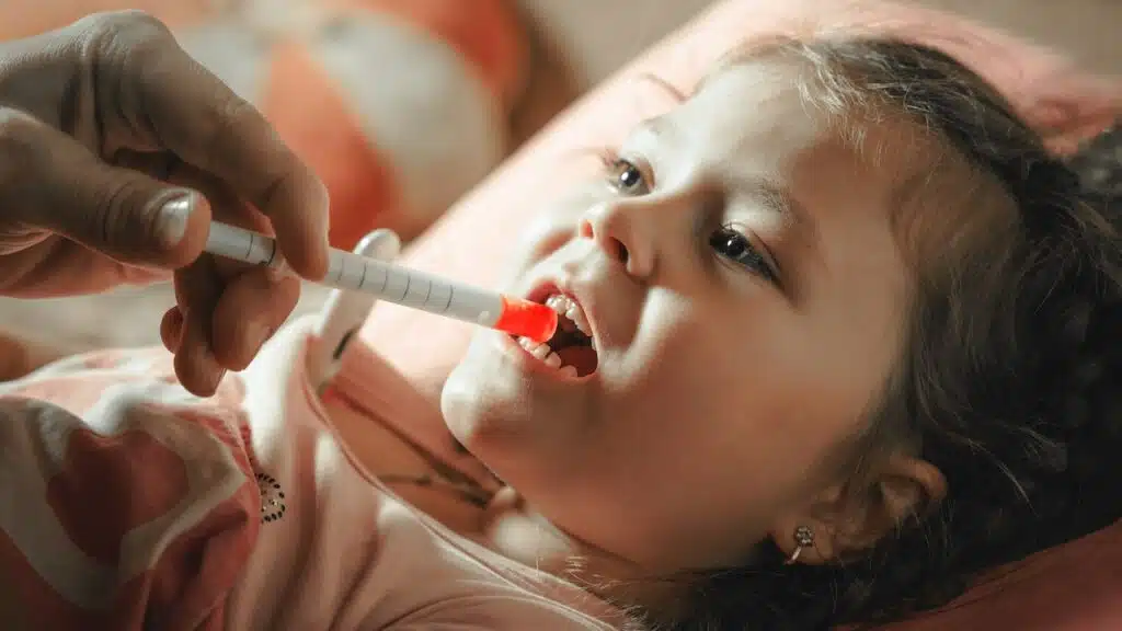 Father giving medicine to sick child with syringe.
