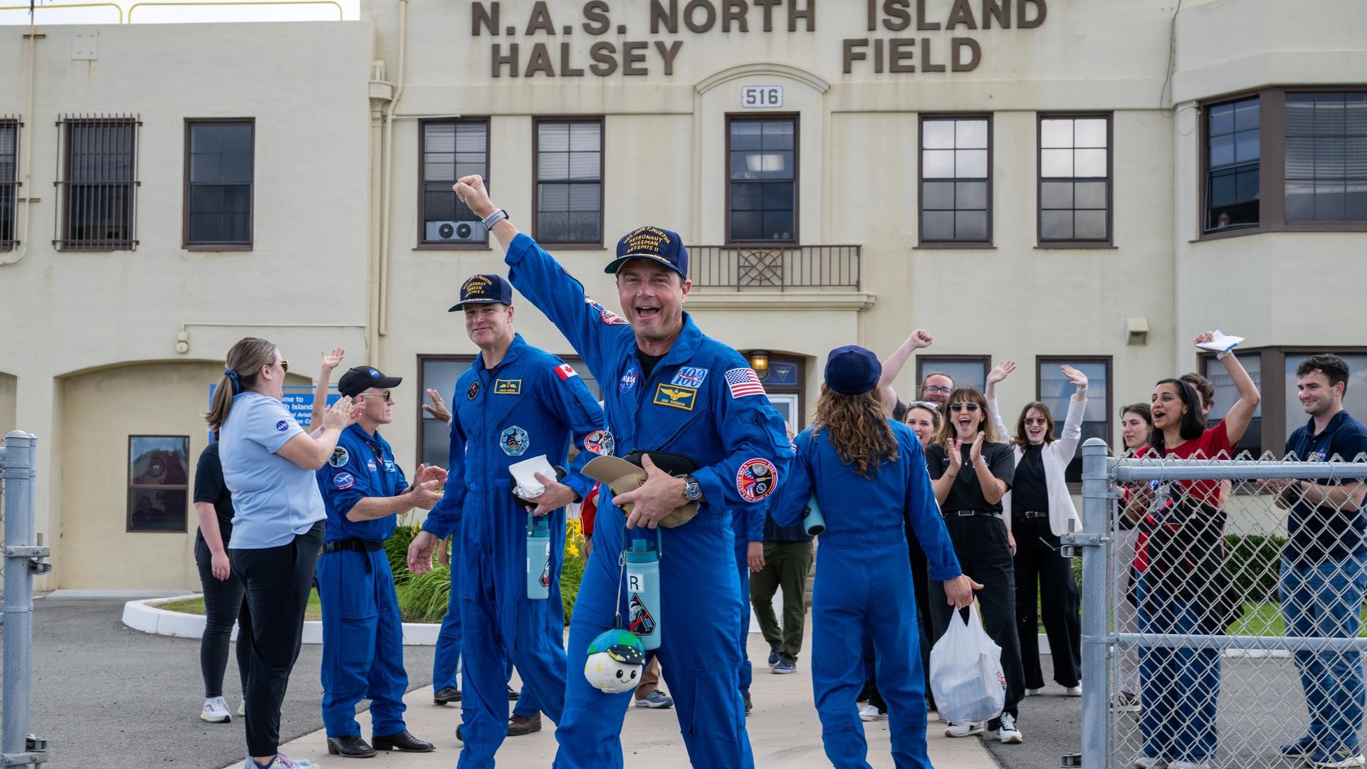 a man in an orange flight suit smiles while carrying a small stuffed moon