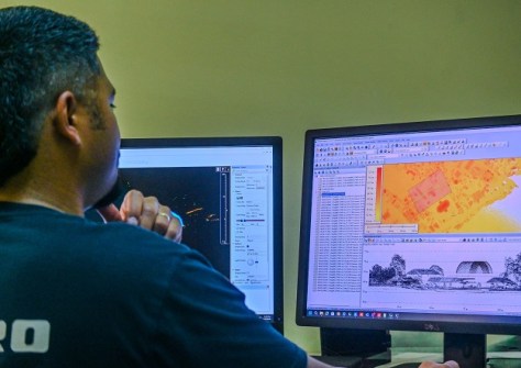 A man sitting at a desk and looking at a computer screen, on which is displayed LiDAR survey mapping data