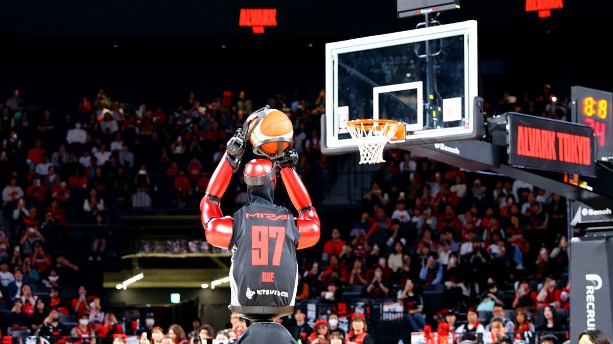 A robot prepares to shoot a basketball in an arena.