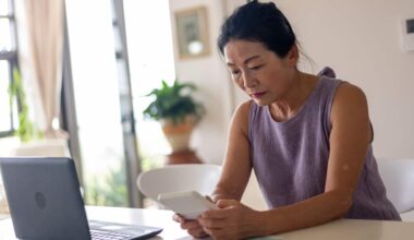 A woman looking stressed with a calculator, laptop and bills sits at a table inside