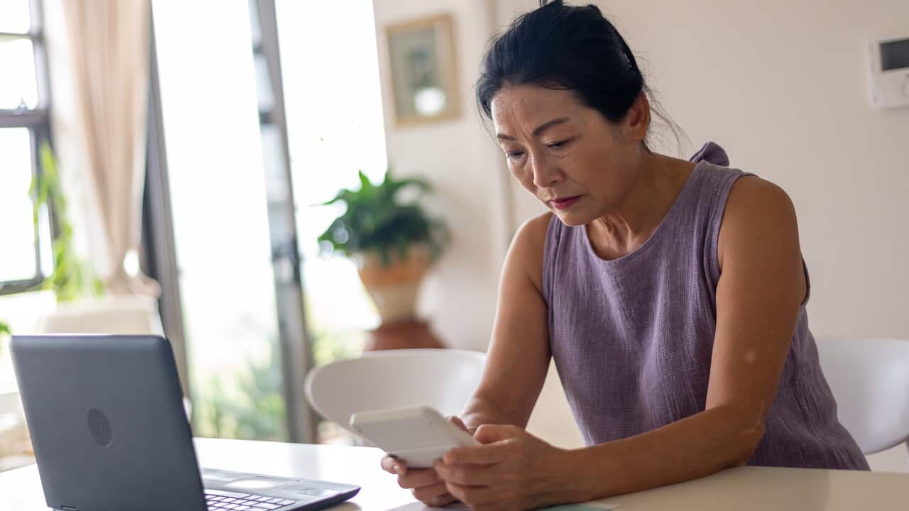 A woman looking stressed with a calculator, laptop and bills sits at a table inside