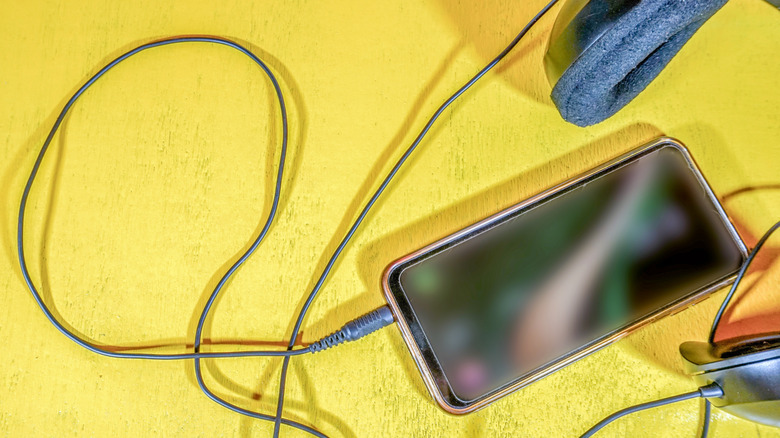 Headphones plugged into the headphone jack of a phone on a yellow background