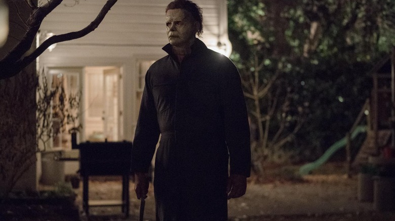 Michael Myers holding a knife by his side in the yard in Halloween (2018)