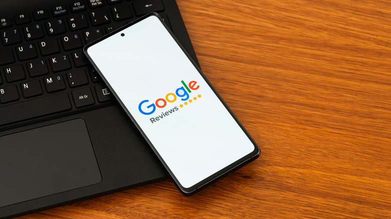 A phone atop a laptop keyboard showing the Google Reviews screen.