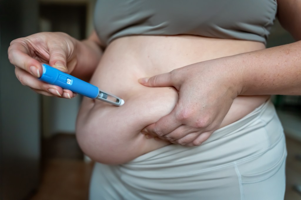 Woman injecting a GLP-1 weight loss medication into her belly fat.