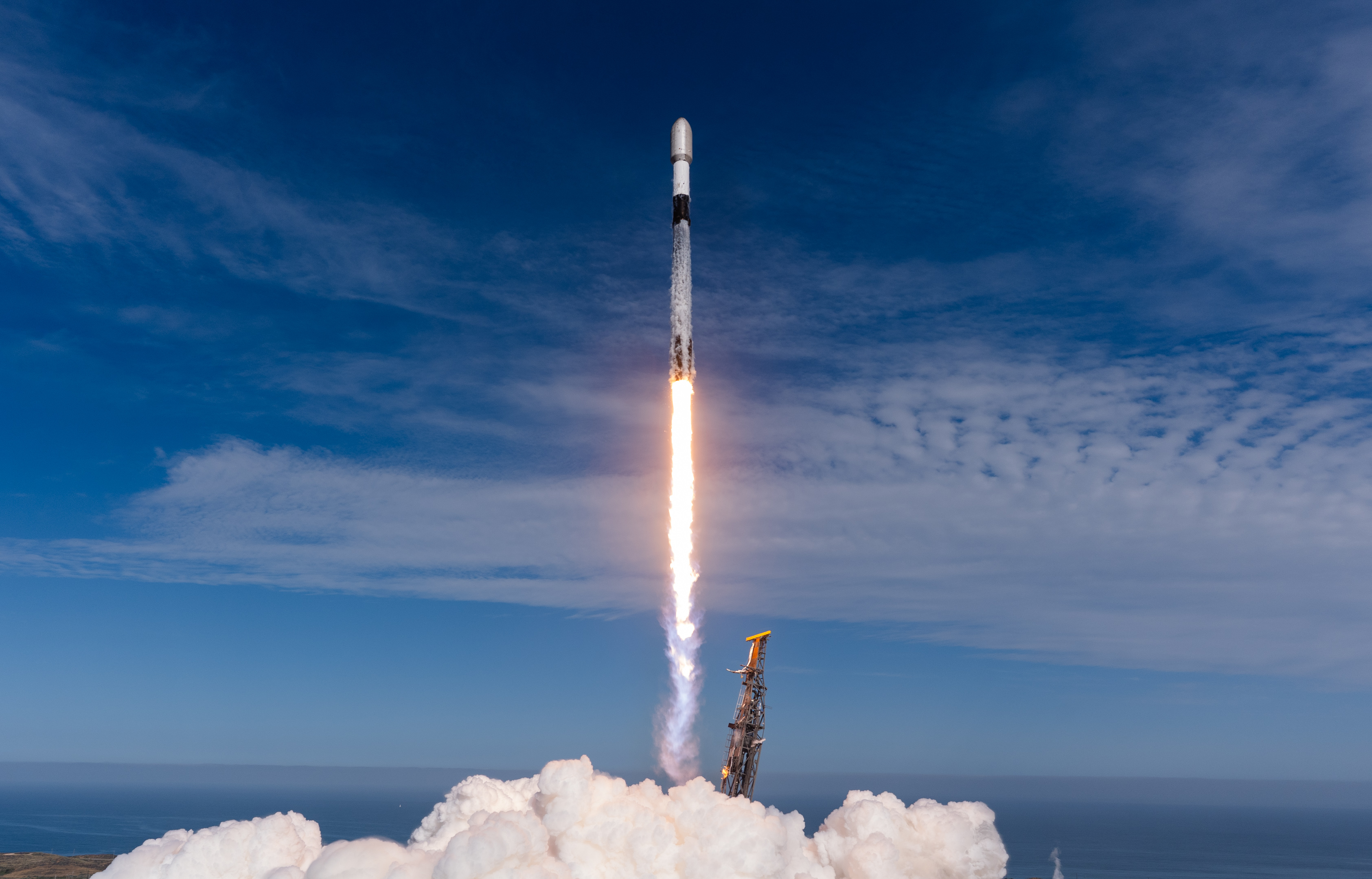 a white and black rocket lifts off into a deep blue sky riding atop a bright orange and white plume