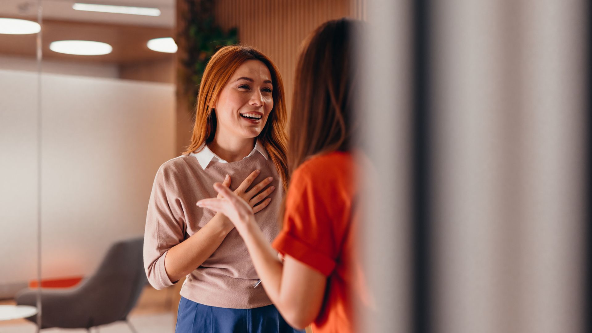 A woman with red hair smiling and laughing while socializing with her colleague