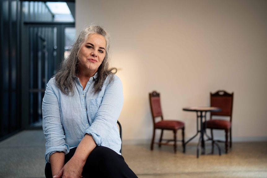 Women with mid-length grey hair sits on a chair and smiles for a photo