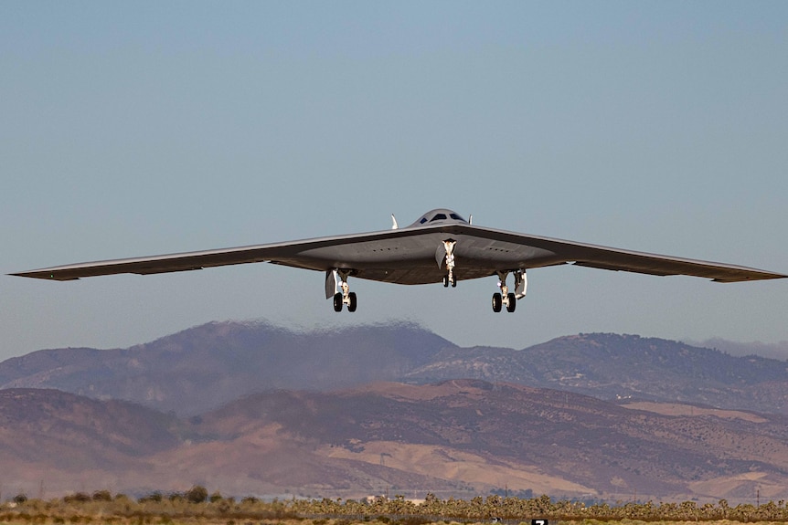An aircraft flies low with mountain ranges in the background.