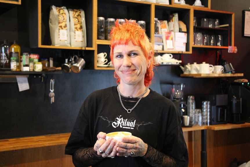 A woman with yellow and red hair smiling while holding a coffee