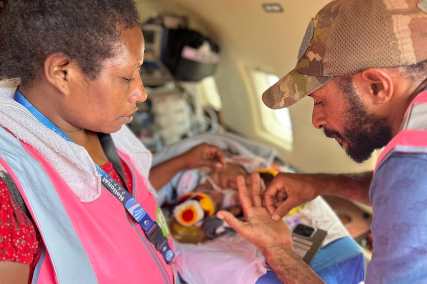 A Papua New Guinean man and woman look at their twins cuddled on a bed.