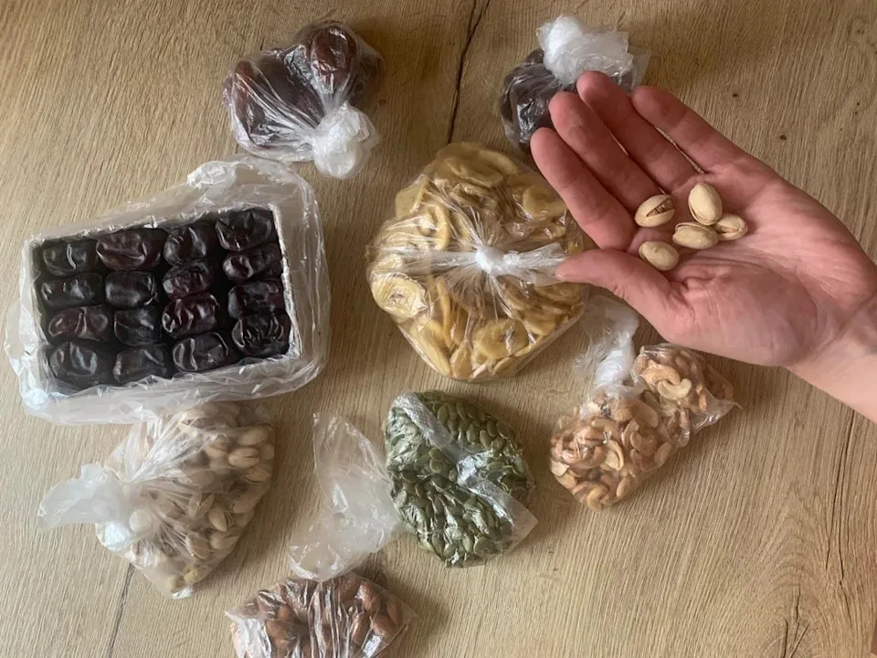 Assorted nuts and dried fruits in bags on a table, with a hand holding pistachios