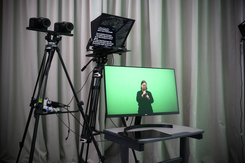 A woman on a monitor on a greenscreen with an autcue in front of her. 