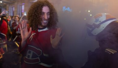 A man in a Canadiens jersey smiles at a police officer in riot gear as they're surrounded by smoke