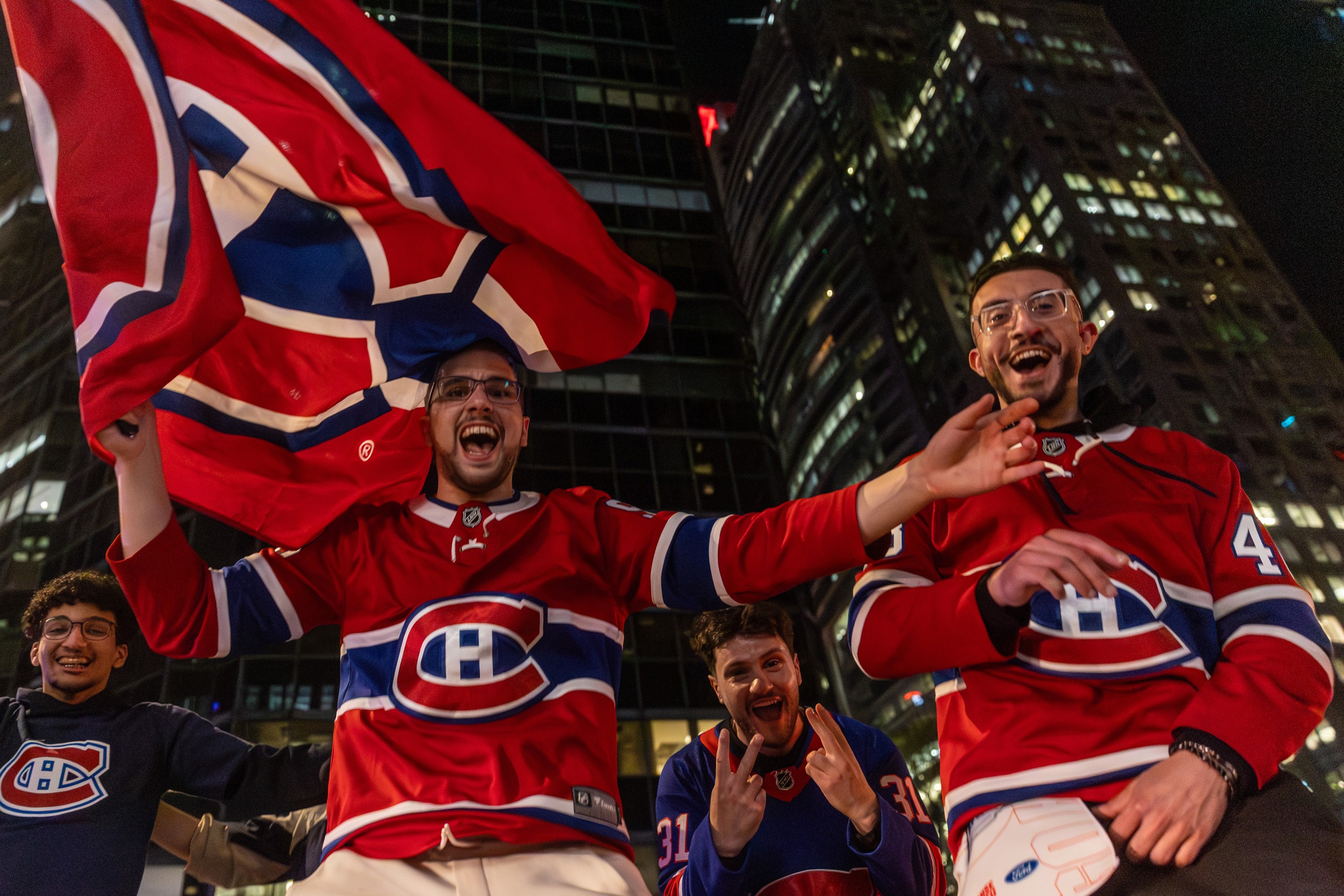 People in Canadiens jerseys and carrying Canadiens flags cheer on a street outside at night.