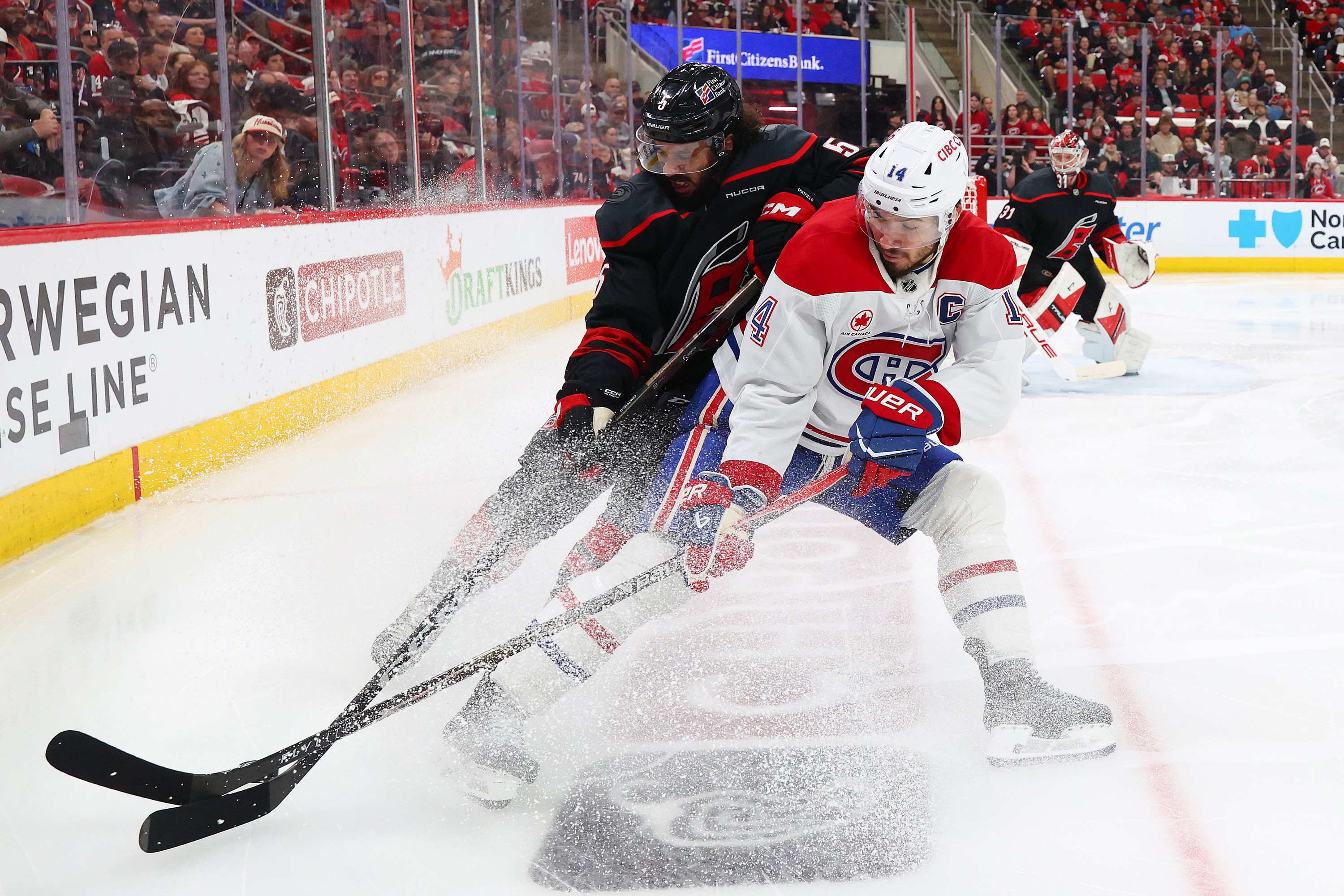 Canadiens' Nick Suzuki battles Hurricanes' Jalen Chatfield for possession.